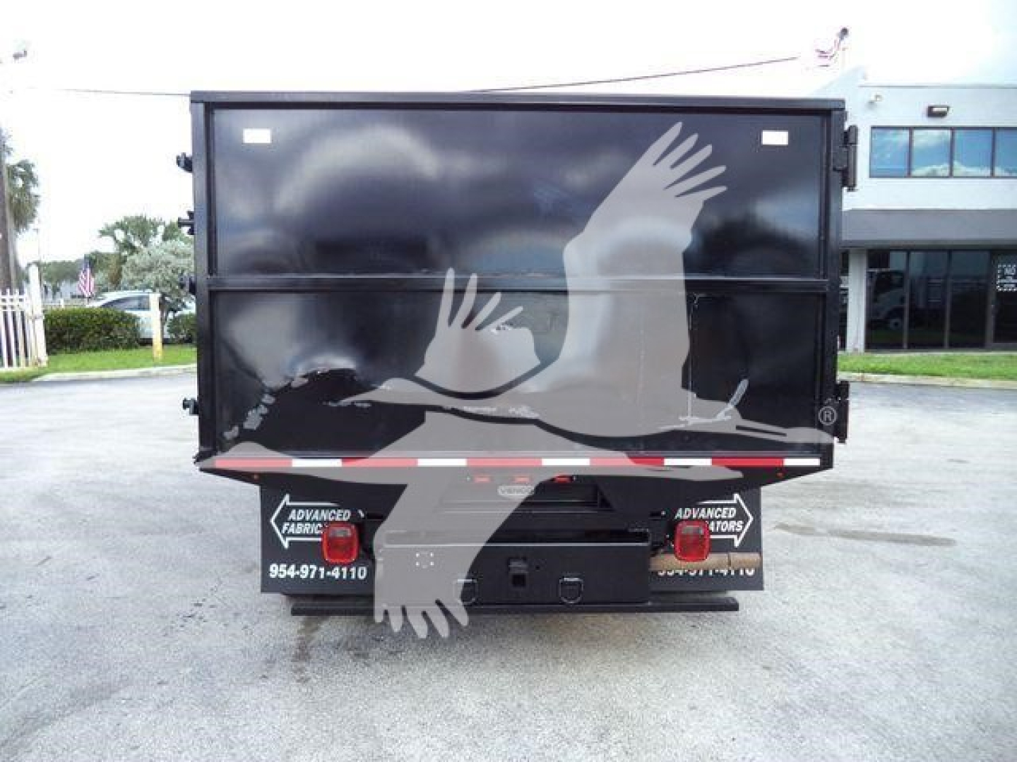 Rear view of a 2011 Ford E450 dump truck showing black dump bed with gull wing logo and taillights; some branding stickers visible near bumper.