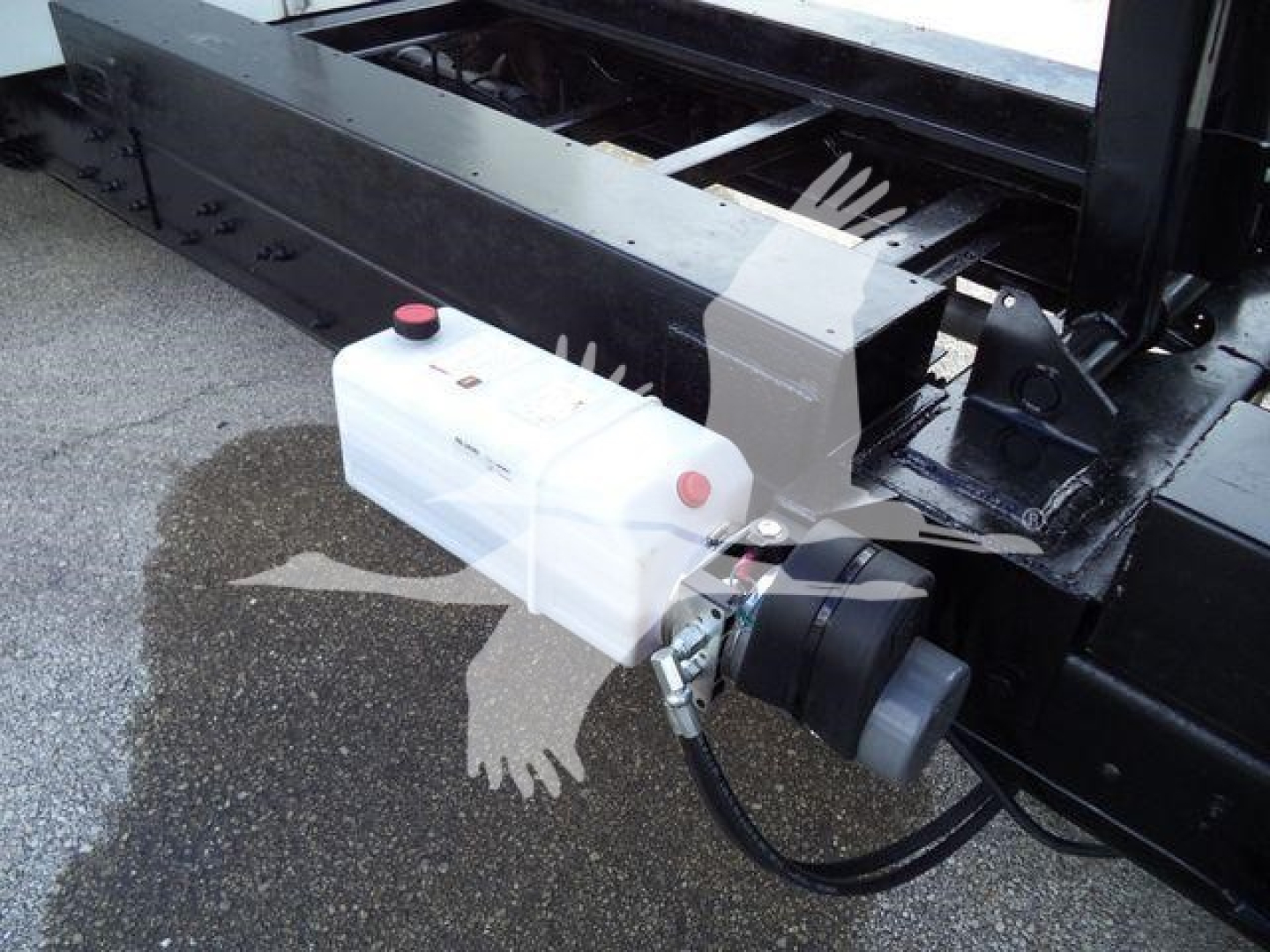 Truck hitch area with white plastic reservoir and hydraulic line connected to black metal frame