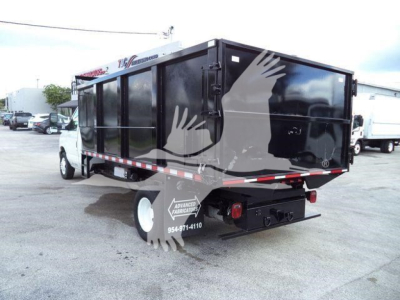 Ford E-450 dump truck with black dump body; rear view showing contact decals and reflective tape; side shows building and lot in background.