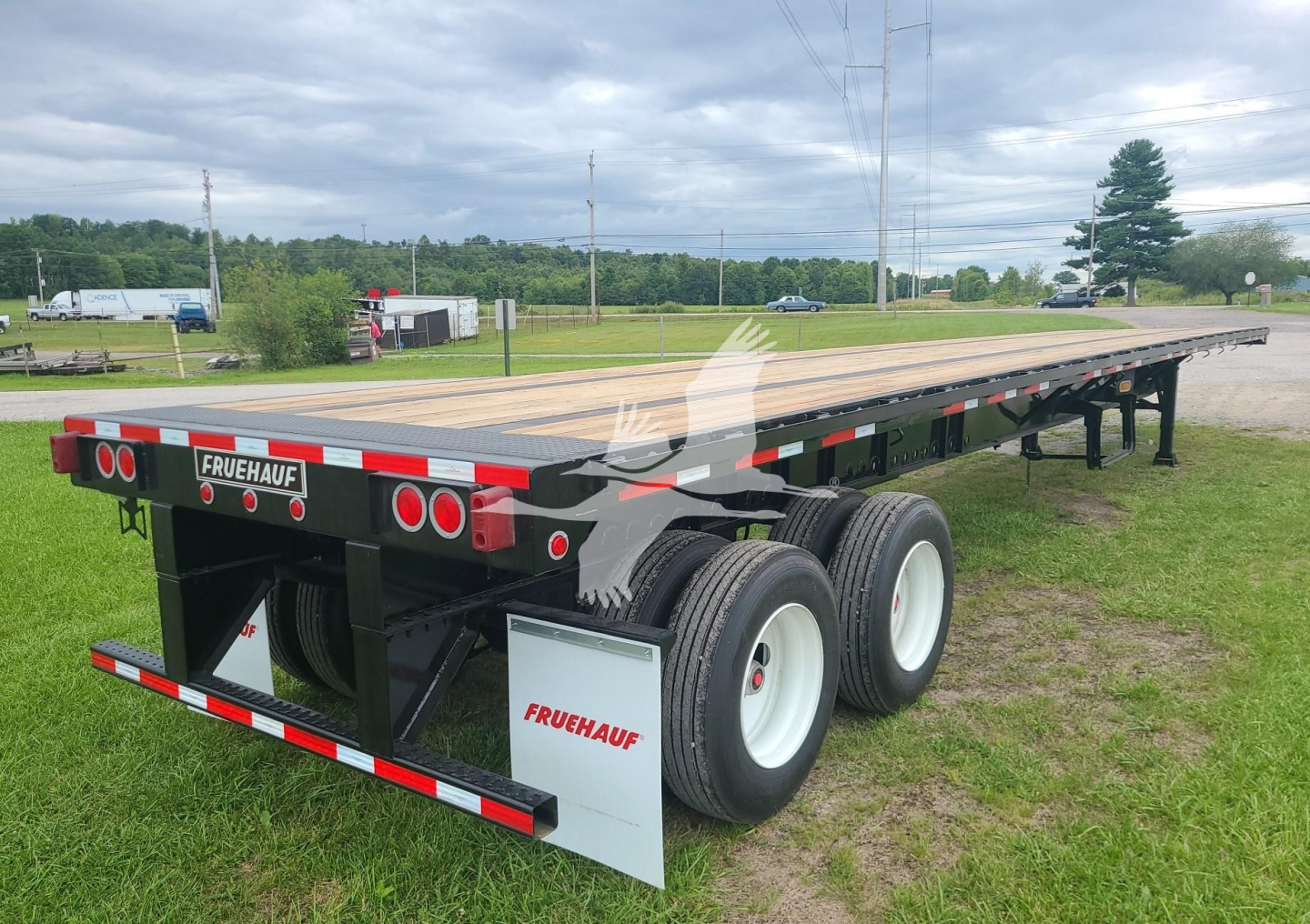 Flatbed trailer with dual rear axles and a Fruehauf brand mudflaps, long spring slider trailer showing reflective red/white tape and certification stickers.