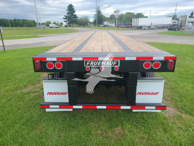 Fruehauf flatbed trailer rear view showing Fruehauf branding and wooden deck with black frame, dual red tail lights, and gray battery boxes on each side.