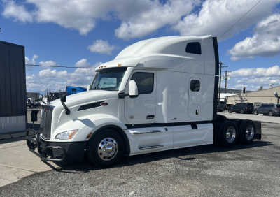Peterbilt 579 tractor-trailer in white, side view, with sleeper cab and chrome wheel rims. Visible front grille, headlights, mirrors, and black bumper. No text legible on the truck or nearby.