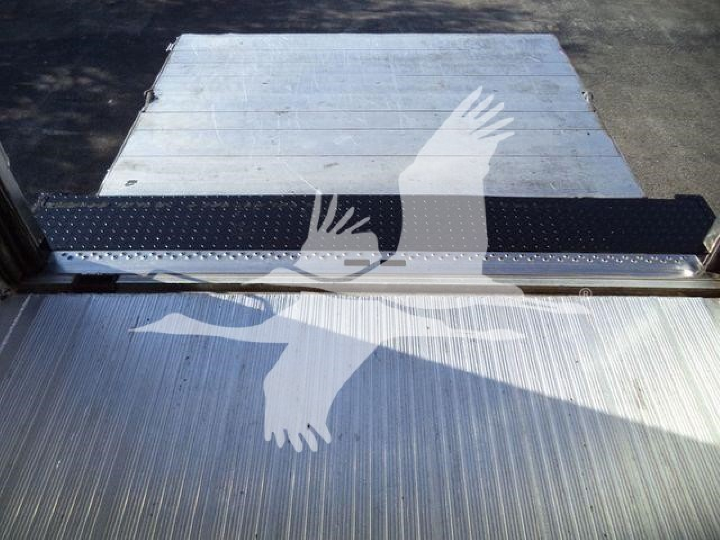 Truck cargo area with aluminum floor and step leading to refrigerated compartment, showing ribbed metal surface and a black non-slip strip.