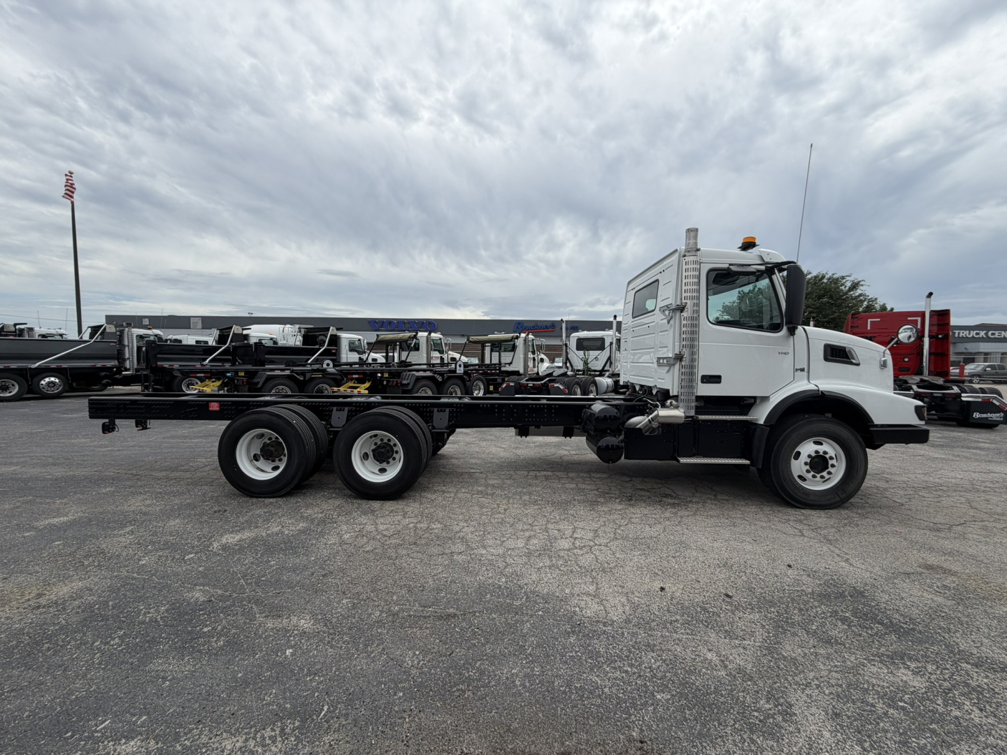 Volvo VHD86B300 cab and chassis truck side view showing triple rear axles and white cab with orange beacon on roof.