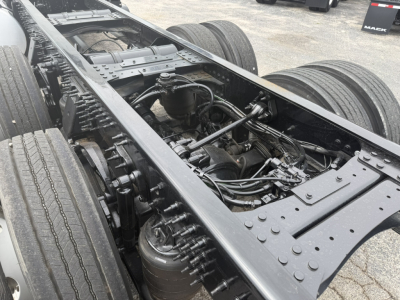 Truck chassis frame with rear dual axles and engine components visible between frame rails; hydraulic hoses and steering linkage present.