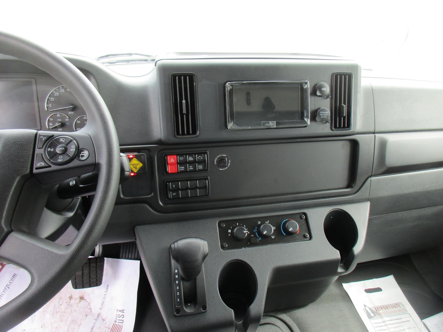 Freightliner M2 106 cab interior showing steering wheel, dashboard, control panel, and center console with cup holders.
