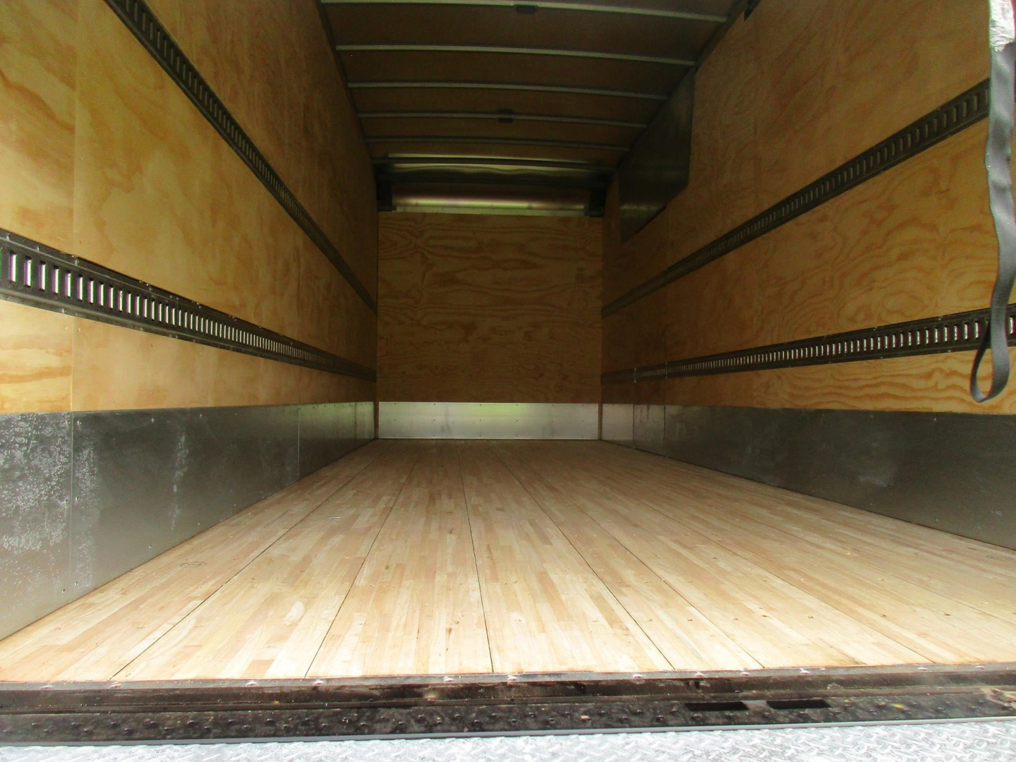 Interior view of a Freightliner M2 106 cargo truck trailer with wooden floor and side rails, empty box area.
