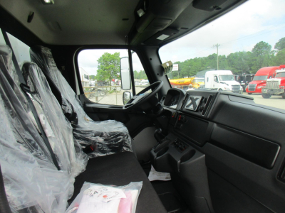 Cab of a new Freightliner M2 106 truck showing front seats wrapped in plastic and dashboard with steering wheel and controls.