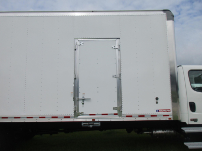 Truck side with box cargo trailer showing rear access door and Freightliner badge.