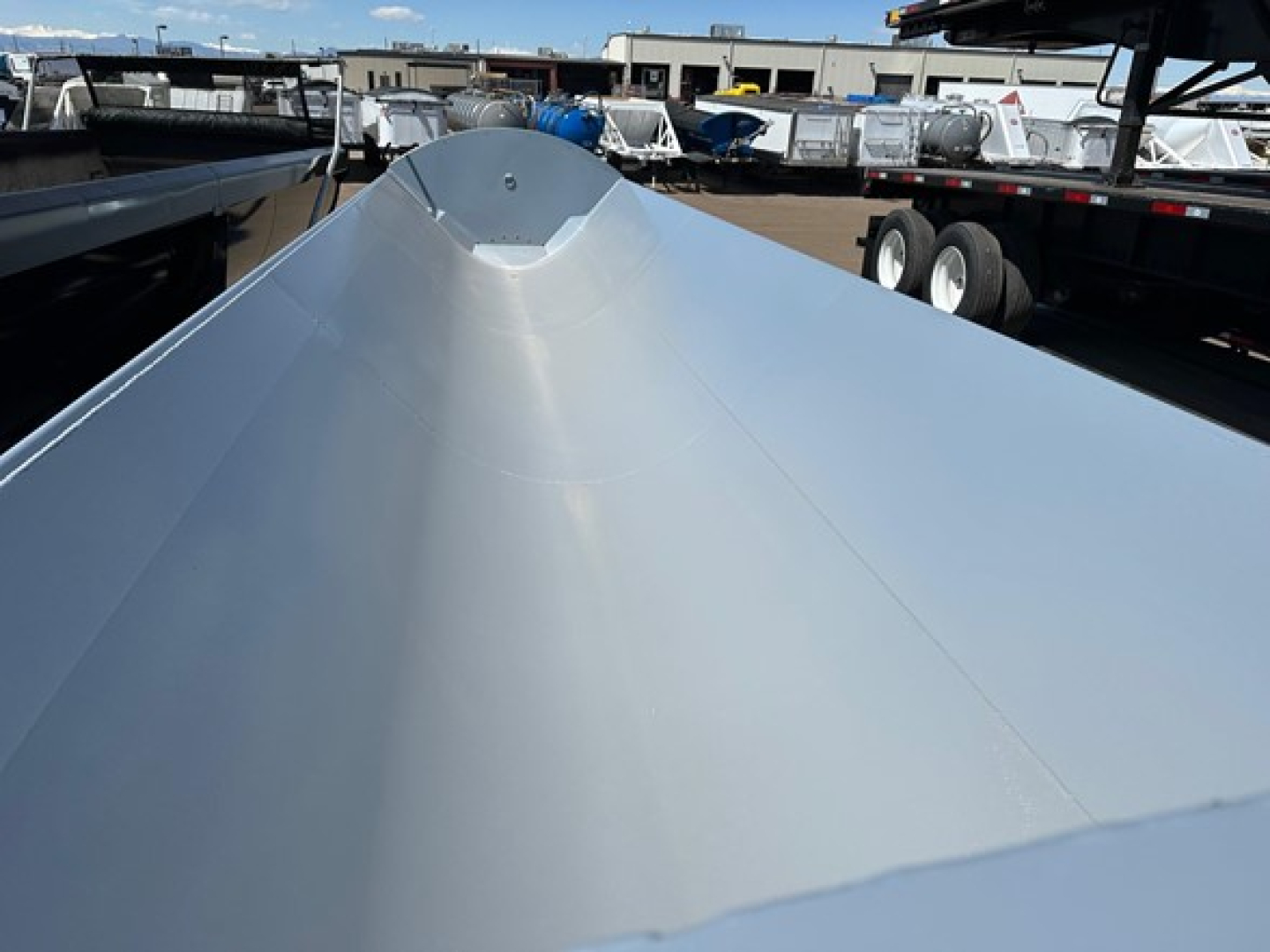 Side dump trailer roof with curved peak and smooth metallic surface, multiple trailers in background.