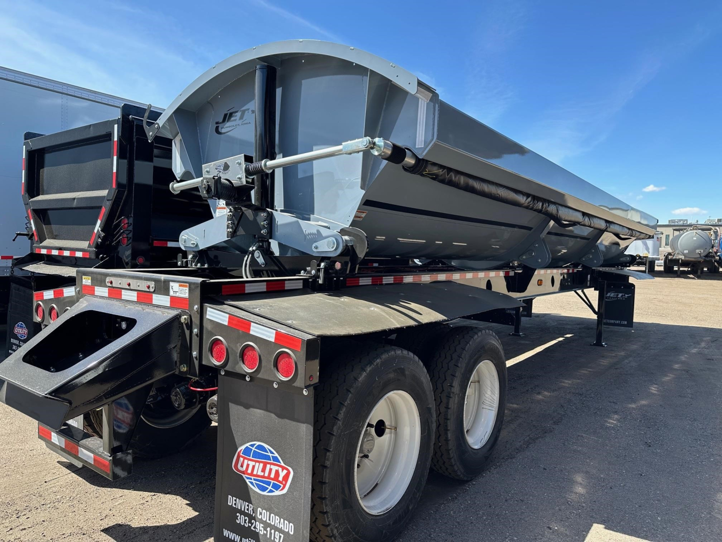 Jet air ride side dump trailer showing hydraulic mechanism and dual rear axles with white wheels.