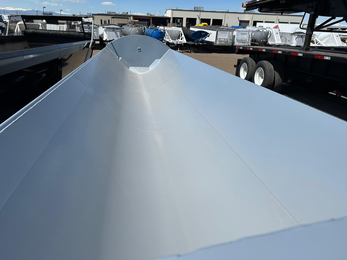 Jet air ride side dump trailer bed with smooth metallic surface, central rounded apex, and parked trailers in background.