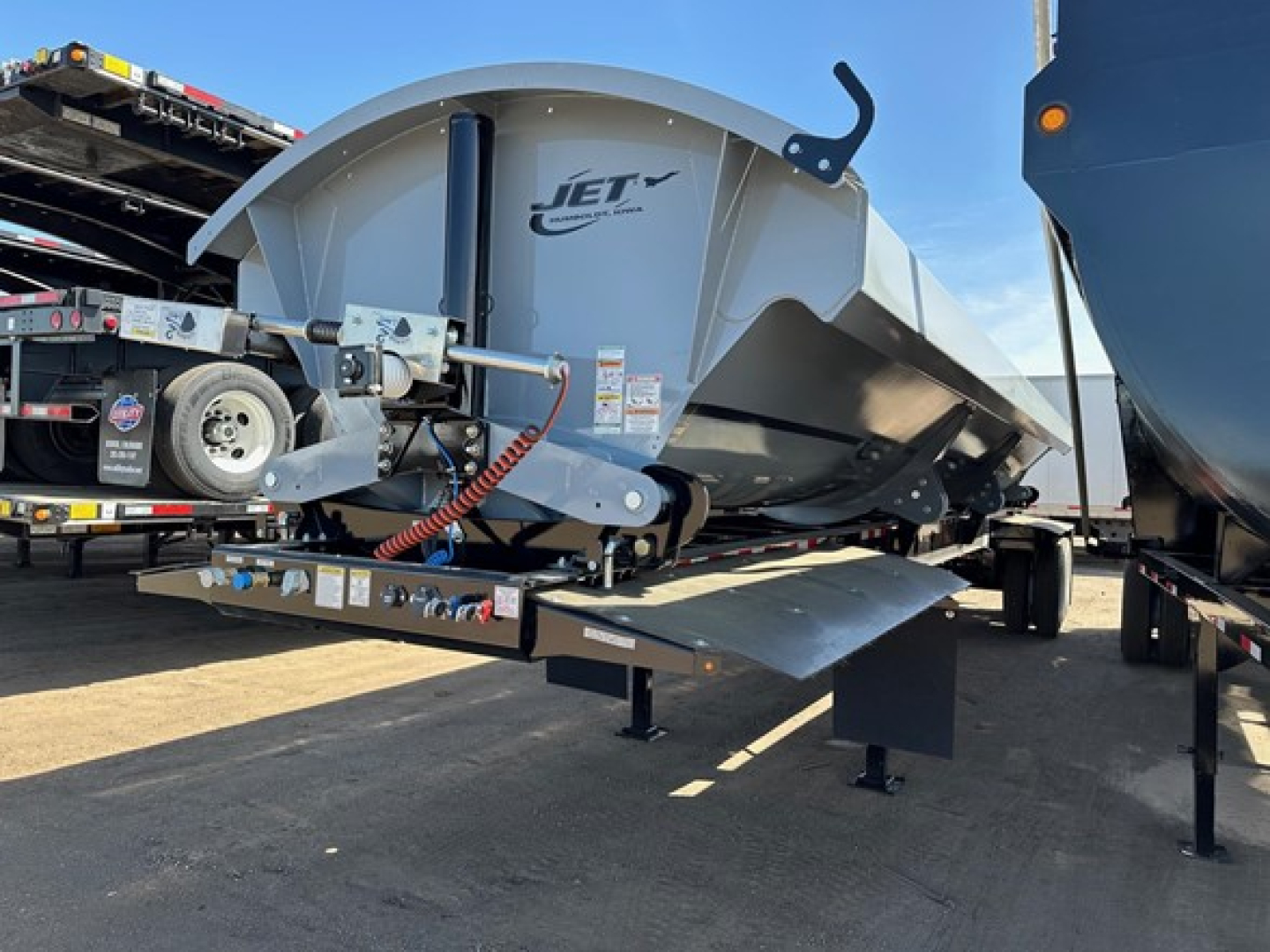 Jet side-dump trailer with front-mounted hydraulic mechanism and curved gray bed, showing Jet brand logo and service components on a trailer deck.