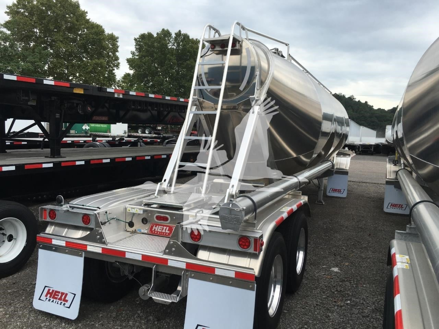 Heil Cementer pneumatic dry bulk trailer viewed from rear-right, polished stainless steel cylindrical tank, ladder and rear coupling with red/white reflective tape, wheels and fenders visible.