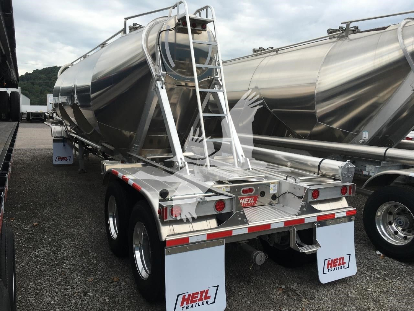 Heil cementer trailer back view showing dual rear axles and ladder with polished aluminum tank, branding plates, and reflective tape.