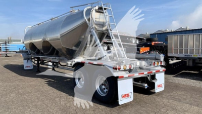 Heil Cementer trailer in a parking lot, rear view showing cylindrical tank with ladder and support frame, dual rear axles, white mud flaps, and brand stickers.
