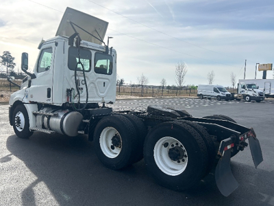 Truck tractor cab provided with a dump/tilt hood open, showing front-left side view and chassis with dual rear axles and fifth wheel. Visible white cab, fuel tanks, and wheels.