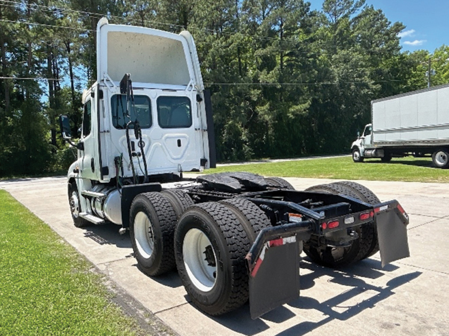 Freightliner Cascadia125 tractor showing rear chassis and dual rear axles with fifth wheel and mud flaps. Cab visible with white paint and large sleeper height, trailer hitch area empty.