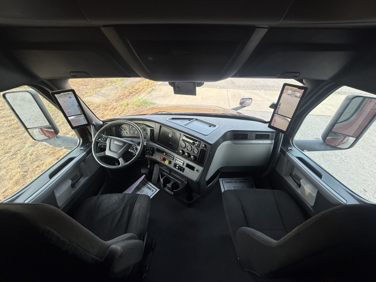 Cab interior of a Freightliner Cascadia 126 truck showing steering wheel, dashboard, and two side mirrors. Text not legible.