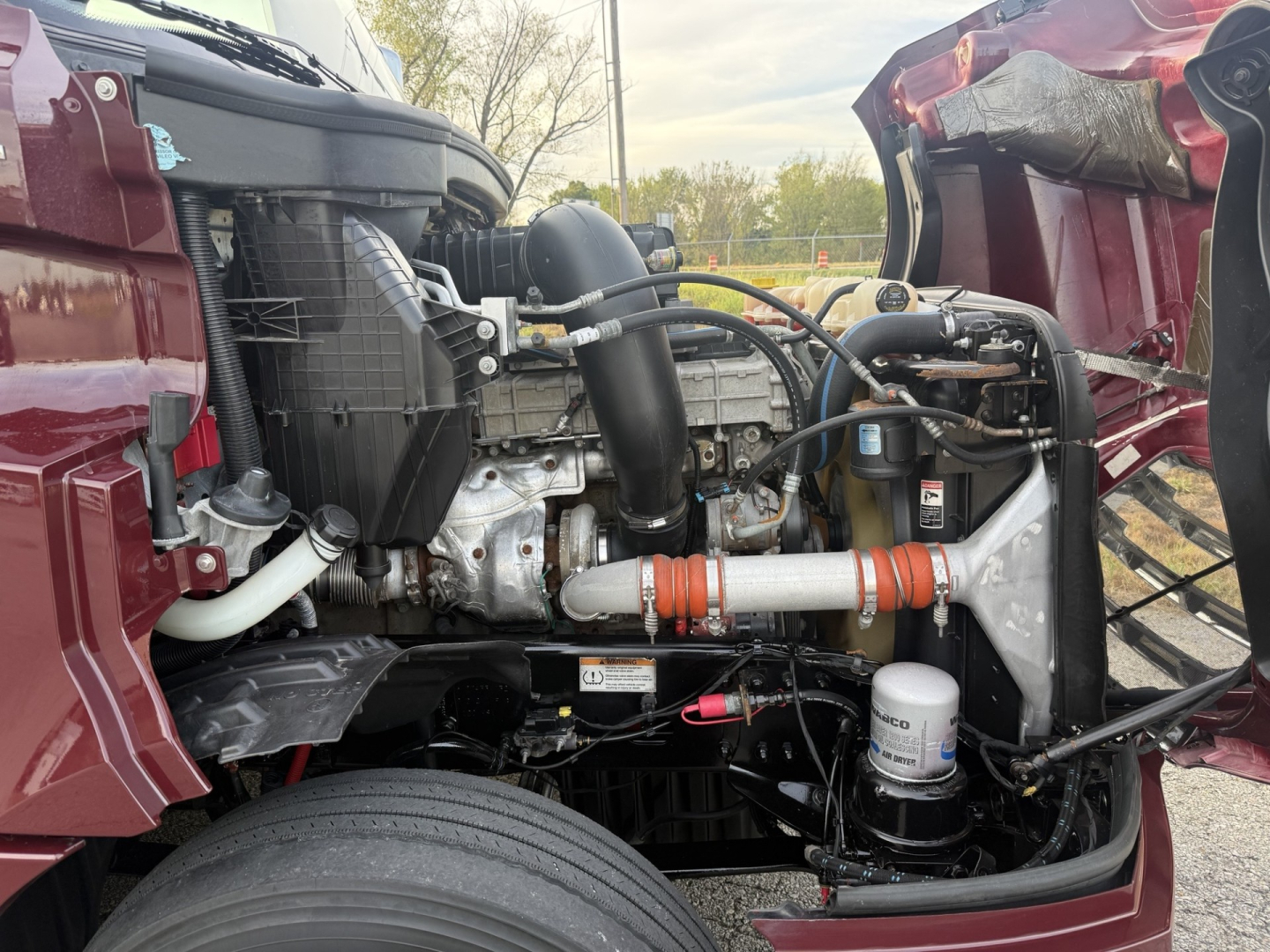 Truck engine bay of a 2021 Freightliner Cascadia 126 showing radiator, hoses, filters, and intake components in red cab with open hood.
