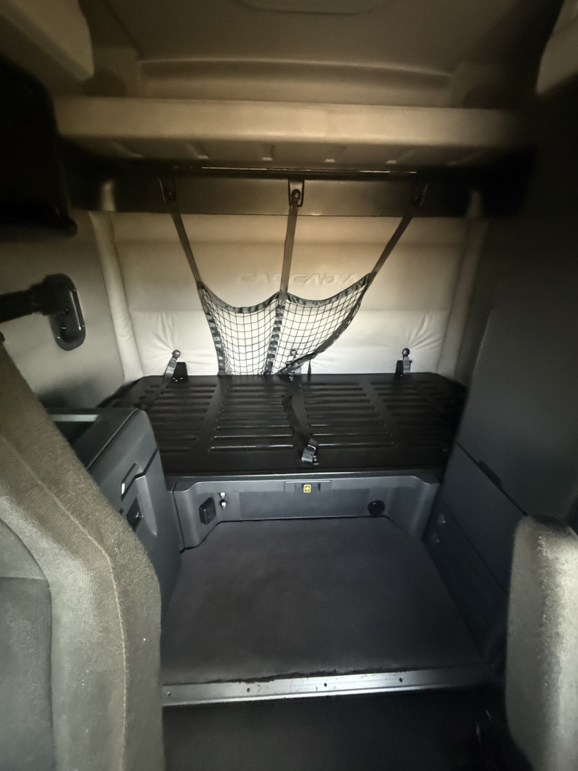 Cargo area of a Freightliner Cascadia 126 sleeper cab with a netted storage area and cargo floor visible.