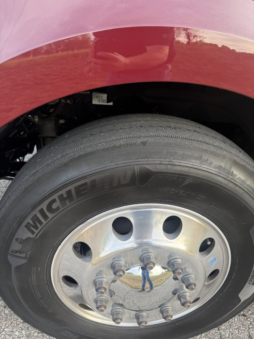 Truck wheel and tire close-up showing Michelin tire on front dual-axle rim with lug nuts and part of red fender.