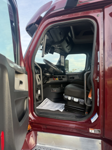 Truck cab interior of a 2021 Freightliner Cascadia 126 with open door, dashboard, steering wheel, and seat visible.