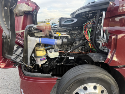 Engine bay of Freightliner Cascadia126 with exposed components including air intake hose, reservoirs, and wiring; blue hose visible.