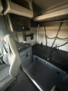 Cab interior of a Freightliner Cascadia sleeper shows bunk area with storage nets, overhead compartment, and seating in view.