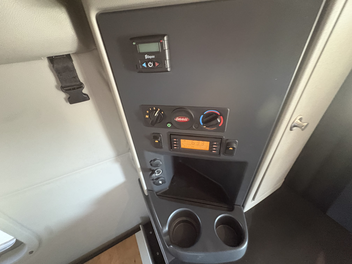 Cab interior of a Peterbilt 579 showing control panel with climate knobs, small display, cup holders, and storage pocket.