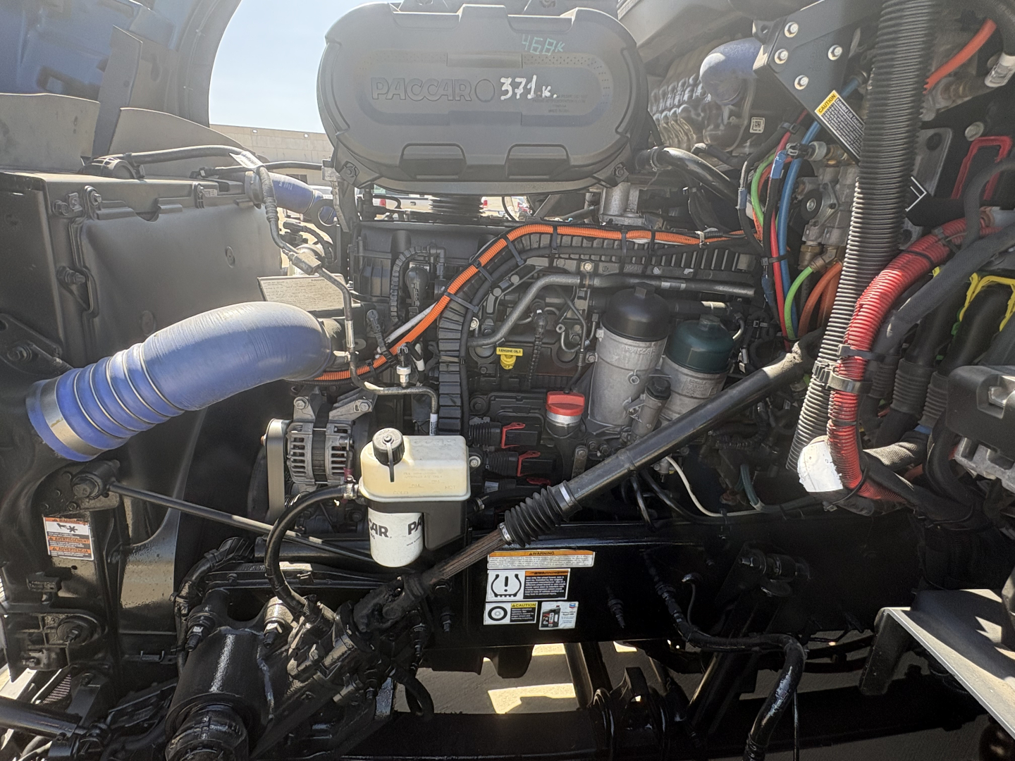 Peterbilt 579 engine bay showing air intake, coolant reservoir, and various labeled fluid lines and wiring harnesses.