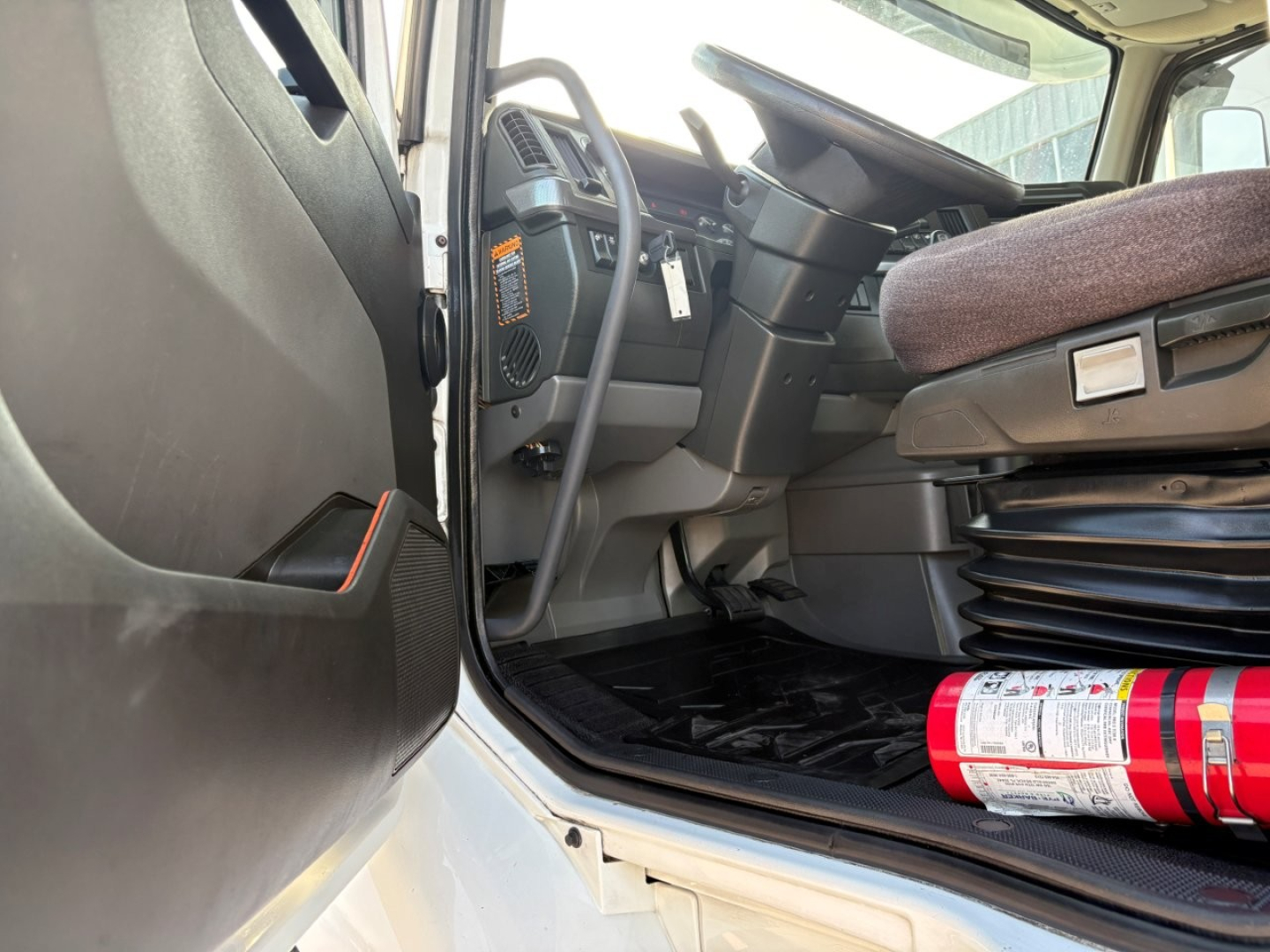 Volvo VNR truck cab interior showing steering wheel and driver's seat with floor mat and fire extinguisher
