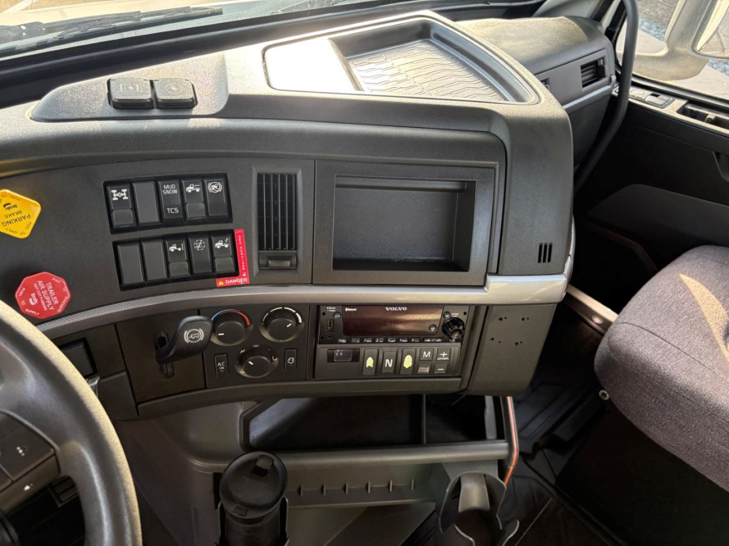 Truck dash and center console with control buttons, knobs, and a small display screen. Visible text includes various control labels and switch legends on the cab interior of a Volvo VNR series truck.