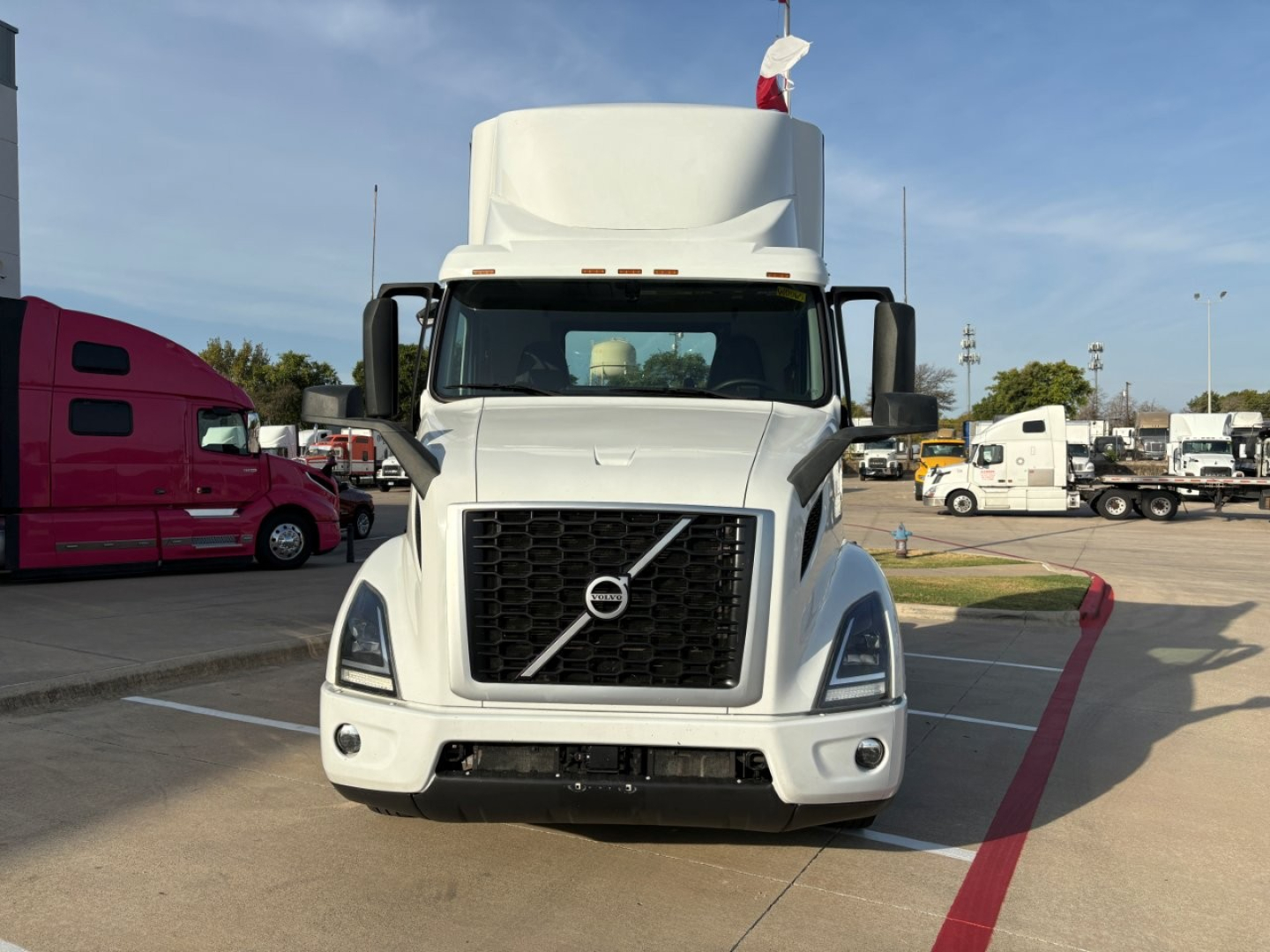 Front view of a white Volvo VNR truck with large black grille, Volvo emblem, prominent bumper, and sleeper cab.