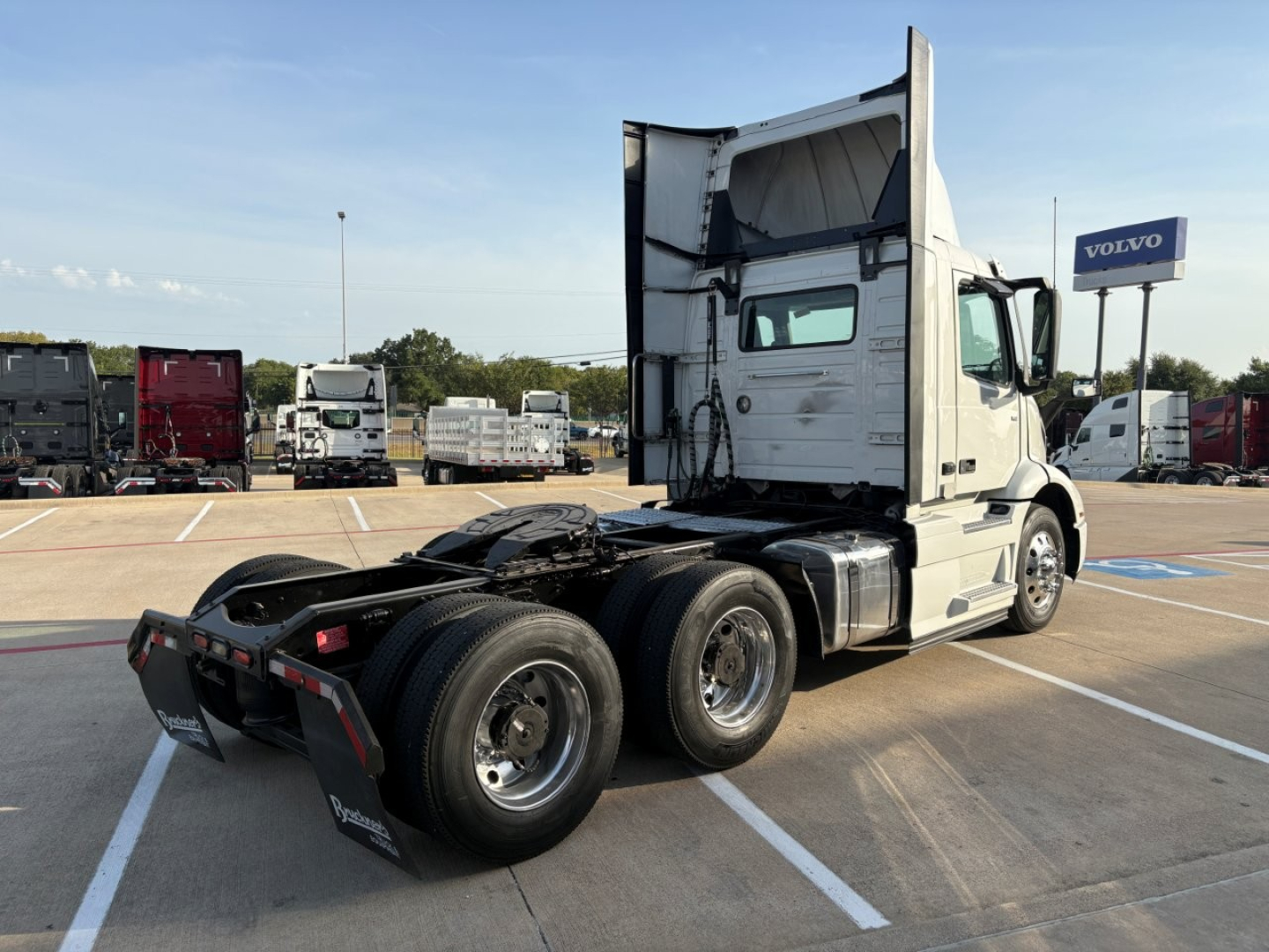 Volvo VNR64T300 truck in a lot showing side rear view with cab raised and triple rear axles.
