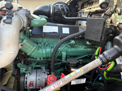 Volvo VNR64T300 engine bay showing diesel engine with green block, black intercooler piping, red oil cap, and warning label on dipstick area.