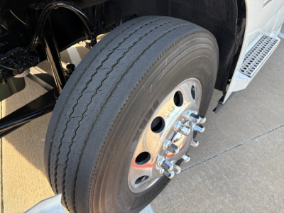 Truck wheel and front suspension of a 2022 Volvo VNR64T300, showing a large front tire with polished steel wheel and multiple lug nuts.