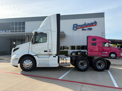 Truck side view showing 3-axle tractor with white cab and chrome fuel tanks in front of a dealership building with 'Bruckeners' sign.
