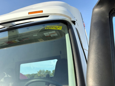 Vehicle cab side view showing windshield with yellow stock tag W0065 and Volvo logo cab interior visible