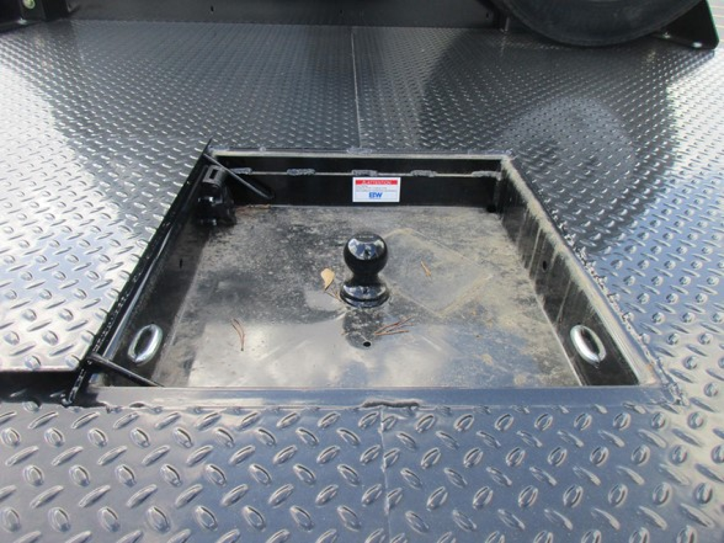 Back of a Ford F-450 flatbed truck showing a square recessed hitch area with a ball hitch and diamond plate steel surface.