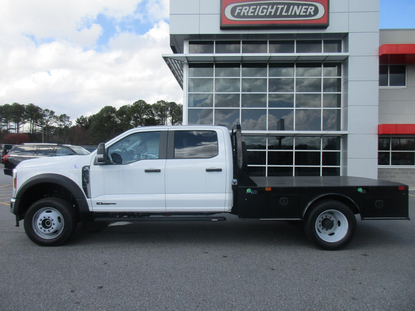 Ford F-450 flatbed truck side view in front of dealership building.