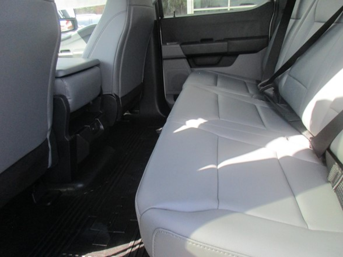 Truck interior rear seating view with light-gray leather seats and black floor mats; rear door panel, seat belt visible.