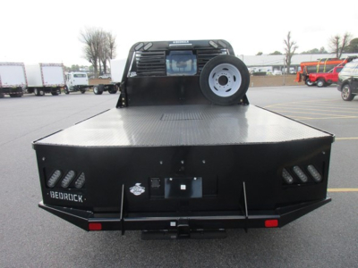 Flatbed truck in rear view showing bed surface, spare tire mounted on cab-back, and dual rear lights with diamond plate surface.