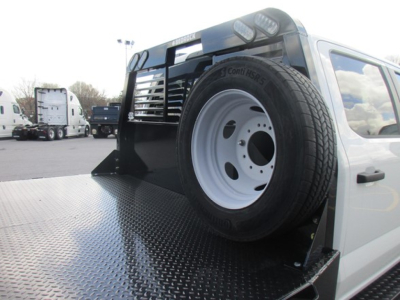 Flatbed tow truck with spare tire mounted on the bed and diamond plate surface; visible text includes Conti tires and wheel details.