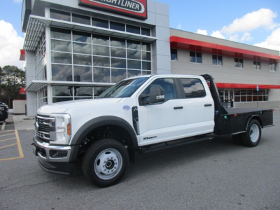 Ford F-450 pickup truck in front of dealership building, white crew cab with flatbed and black utility bed, dealership signage visible.