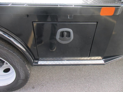 Ford F-450 truck side panel showing storage door with circular recessed handle, black body, diamond plate step trim and wheel visible.