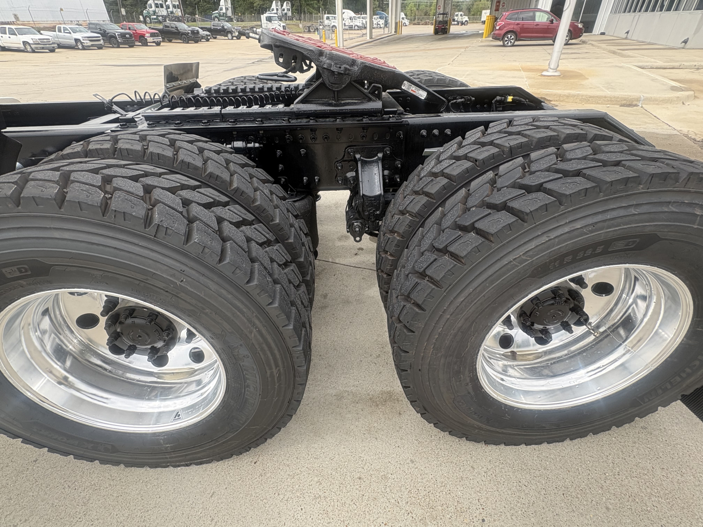 Conventional daycab truck chassis showing dual rear axles with large tread tires and polished rims.
