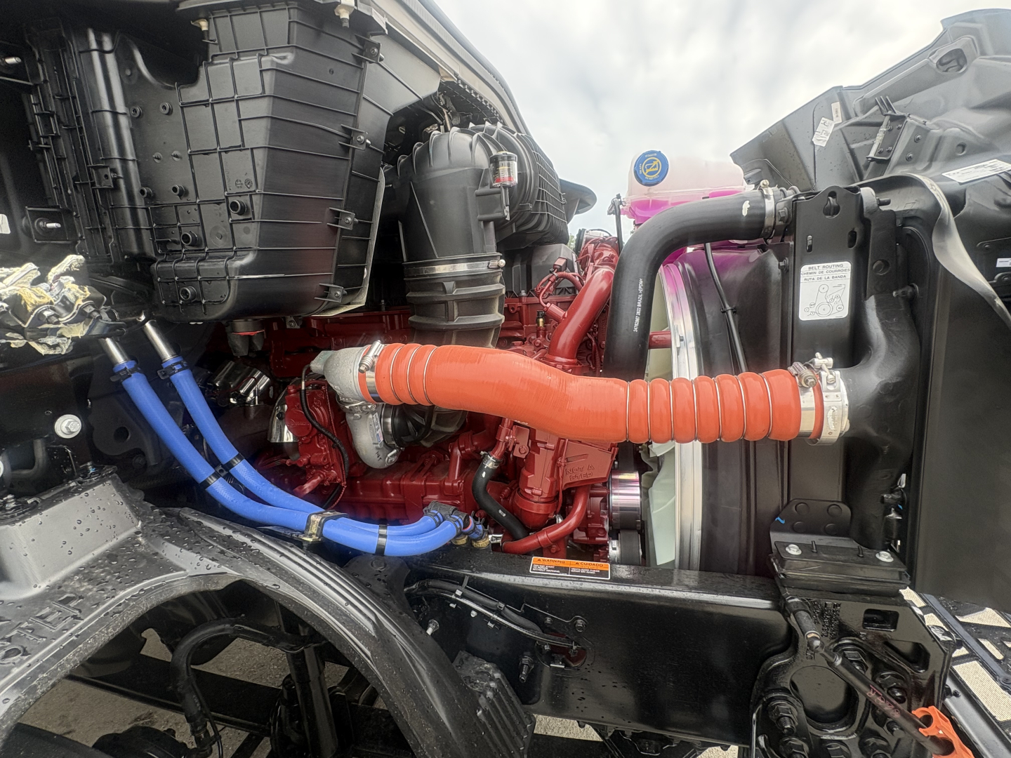 Mack AN64T64 truck engine bay showing orange coolant hose, blue hoses, black air intake, radiator, and red engine components.