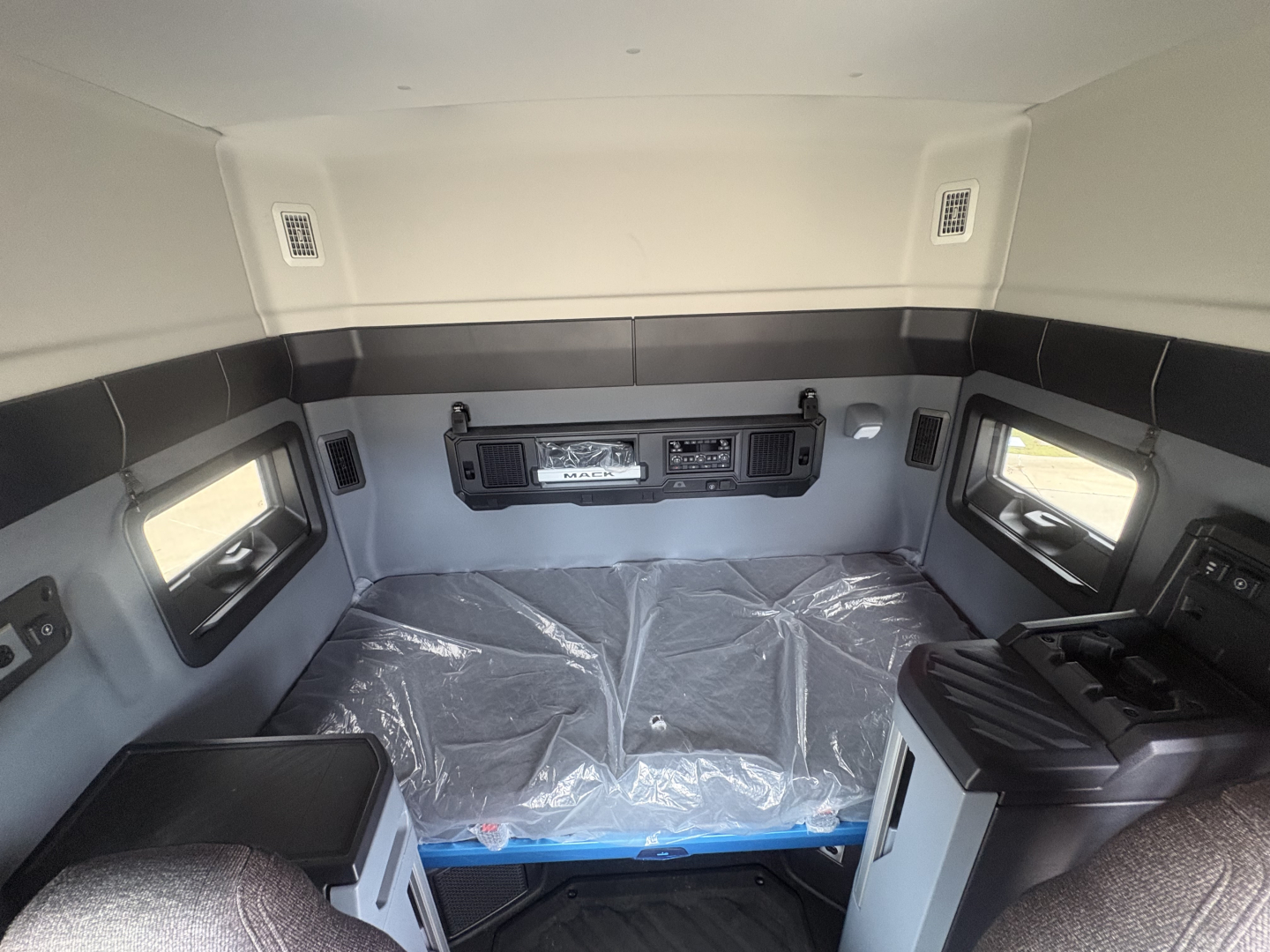 Mack AN64T64 conventional daycab interior view showing sleeper berth with plastic protective cover, control panel, and side windows.