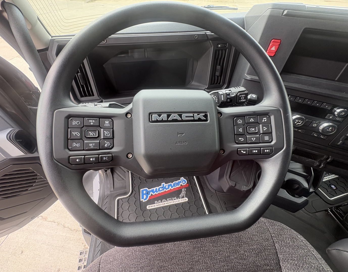 Mack AN64T64 truck interior steering wheel with dashboard controls and Bruncrop? floor mat showing Mack logo.